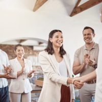 Business handshake with applauding workers in background. Professional company owner shaking hands .